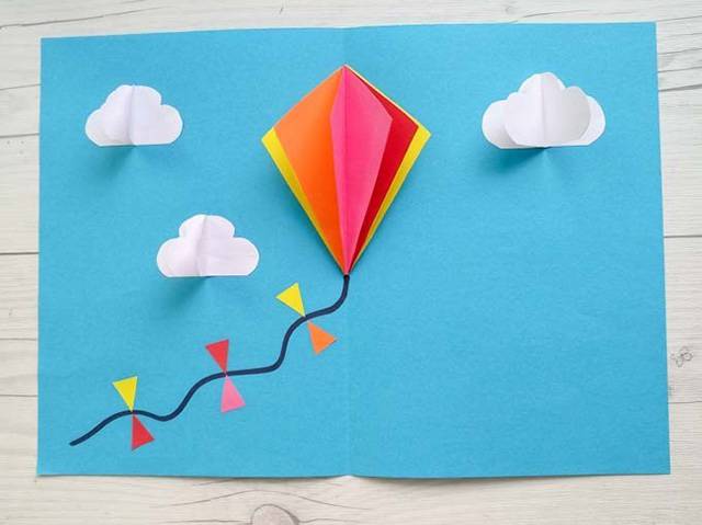 剪纸贴风筝做卡片的方法和步骤5，将风筝粘在天蓝色卡纸的折线上，这样卡纸打开或者折叠的时候，风筝也可以跟着开合。