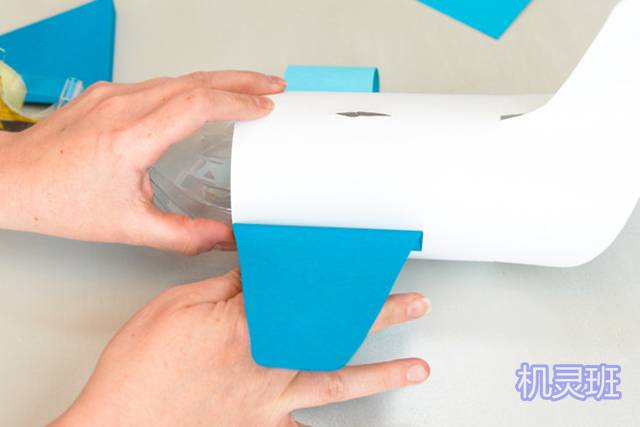 回收利用矿泉水瓶做存钱罐的步骤7，把多出来的一厘米折叠到和翅膀垂直，涂上胶水后粘在瓶身两侧。