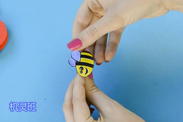 母亲节手工心形花朵贺卡制作步骤10，将小蜜蜂用胶带贴在回形针上(示范中用的是小木夹子，你如果手头有，也可以用，只要用胶水将蜜蜂粘在木夹子一侧即可)。