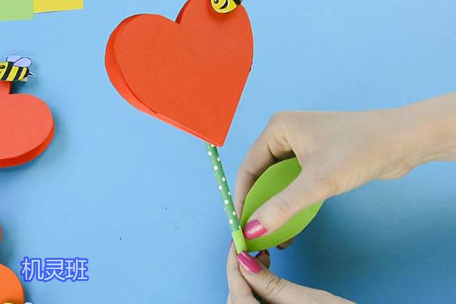 母亲节手工心形花朵贺卡制作步骤13，用绿色的纸张剪下一片叶子形状，粘在吸管上。